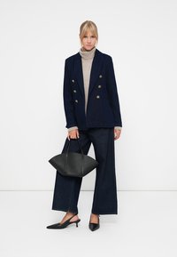 Mørkeblå dobbeltknappet blazer, beige turtleneck, mørke vide jeans, svarte spisse leiligheter og en svart buet håndveske. Enkelt design.