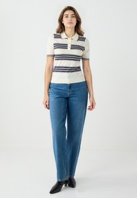 Strickpolo in Creme mit marineblauen und burgunderroten Streifen, mit einem Kragen und kurzen Ärmeln. Kombiniert mit hochtaillierten blauen Jeans und schwarzen Stiefeln.