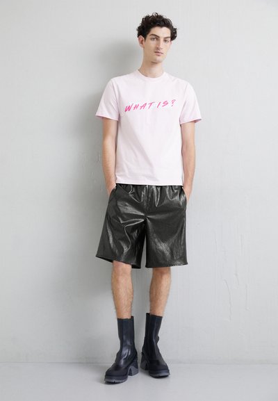Lys rosa bomull t-skjorte med teksten "HVAD ER?", kombinert med skinnende svarte faux skinnshorts og kraftige svarte platåsko.