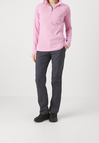 Rosa fleece-tröja med kvartsyggelkrage, i kombination med mörkblå utomhusbyxor. Svarta skor fulländar outfiten.