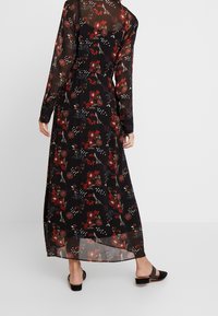 Schwarzes Maxikleid mit langen Ärmeln, das mehrfarbige Blumenmuster zeigt, aus transparentem Stoff gefertigt und mit einer taillierten Taille versehen. Mit dezenten Details akzentuiert.
