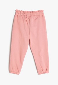 Pantalones de chándal de algodón rosa con cinturilla elástica, piernas ajustadas y puños fruncidos en los tobillos. Textura suave, diseño casual.