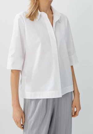 Camisa blanca de manga corta con cuello, que presenta una tapeta y un ajuste relajado. Tejido liso, diseño minimalista y sin patrones visibles.