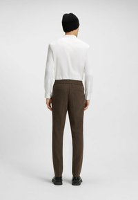 Brown patterned trousers with a relaxed fit, featuring a drawstring waist, two back pockets, paired with a white collared shirt and black beanie.