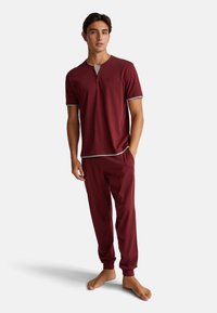 Bordový pyžamový set s tričkem krátkého rukávu, které má šedý výstřih a knoflíkovou légou, doplněný o odpovídající kalhoty s elastickými manžetami.