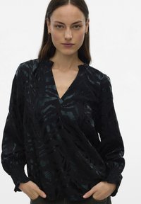 Zwarte blouse met subtiel, getextureerd golfpatroon, V-halslijn en gerimpelde kraag. Lange mouwen met gerimpelde manchetten. Lichtgewicht stof.