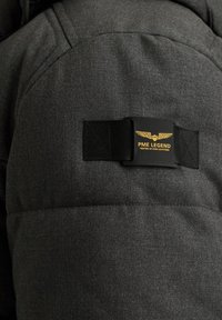Siva podložena jakna z teksturirano tkanino, poševnimi šivi in črno oznako z zlatim napisom "PME LEGEND" ter obliko krila.