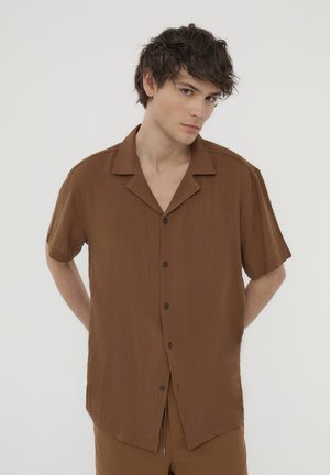 Camicia a maniche corte marrone con bottoni, realizzata in tessuto testurizzato, con colletto a punta e bottoni marroni, caratterizzata da un'apertura frontale.