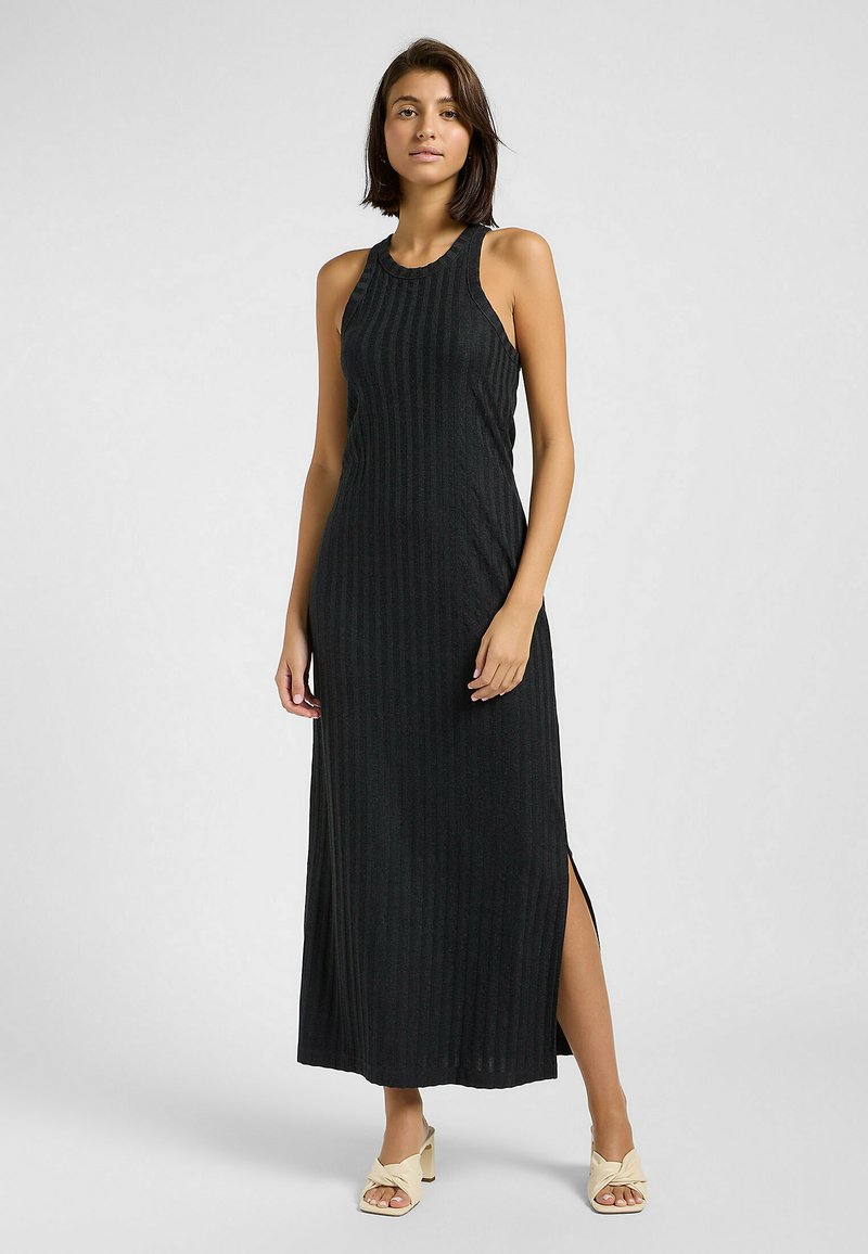 Abito maxi nero a costine con design senza maniche, spacchi laterali e scollo rotondo. Tessuto morbido e silhouette aderente. Indossato con tacchi di colore chiaro.