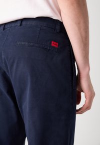 Marineblauwe chinos met een gladde textuur, met een rode "HUGO" label op de achterzak en een standaard taillebandontwerp.