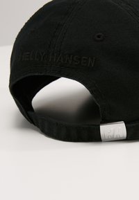Gorra de algodón negra con el bordado "HELly HANSEN" en la parte trasera, que presenta un acento metálico plateado con el logo "HH" en el cierre.