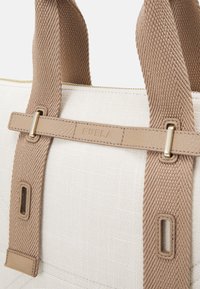 Beige canvas handtas met getextureerde beige riemen en hardware in goud kleur. Bevat een opvallend reliëf merklogo en een ritssluiting.