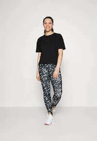 T-shirt preta cropped combinada com leggings pretas apresentando um padrão floral branco. A modelo usa sapatilhas brancas com detalhes vermelhos.