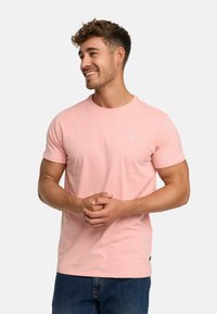 Light pink cotton t-shirt with a crew neck, short sleeves, and a small logo detail on the chest. Paired with blue denim jeans.