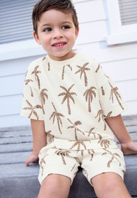Set od lagano žute košulje i kratkih hlača s printom smeđeg palminog drveta. Kratki rukavi, ležerni kroj, mekana pamučna tekstura.