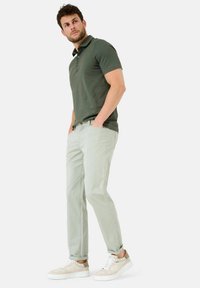Donkergroen poloshirt, lichtgroene broek en beige sneakers. Het poloshirt heeft korte mouwen en knopen. De sneakers hebben lichte accenten en veters.