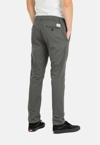 Pantalones gris claro de corte slim para hombre con cintura elástica, dos bolsillos laterales y un bolsillo trasero asegurado con un botón. Tejido de algodón suave.