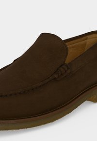 Mocassin marron en cuir à enfiler avec couture visible et semelle en crêpe, vu de profil sur un fond uni.