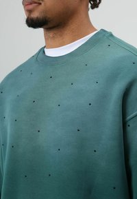 Groene sweatshirt met een ronde halslijn, bezaaid met kleine zwarte versieringen aan de voorkant. Gemaakt van een zachte katoenmengeling.