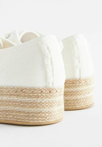 Valkoinen teksturoitu kangasplattoni kengät, joissa on kudottu juuttipohja ja paksu beige naru koriste. Pyöristetty takatyyli, jossa on ompelu detail.