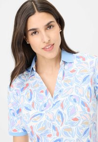 Polo a maniche corte con un motivo a foglie blu su sfondo bianco, con colletto azzurro chiaro e un sottile design a V.