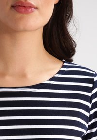 Niebiesko-biały pasek z okrągłym dekoltem, wykonany z miękkiego materiału. Posiada dopasowany krój w okolicach szyi i ramion.