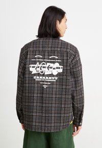 Chemise en flanelle à carreaux dans des tons sombres, avec un imprimé graphique au dos. Manches longues, fermeture à boutons sur le devant et coupe décontractée.