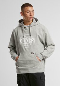 Szürke kapucnis pulóver, puha anyagból készült. Elől zsebes, húzózsinóros kapucnival rendelkezik, a mellrészen a "DICKIES" felirattal ellátott logó található.