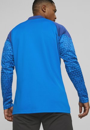 Hemd mit langen Ärmeln für Herren in leuchtendem Blau, mit strukturiertem Stoff an den Ärmeln, das geometrische Muster in dunklerem Blau auf Schultern und Armen aufweist.