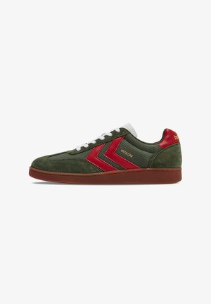 Green suede sneaker with red accents, featuring a white textured tongue, brown rubber sole, and diagonal stripes on the sides.