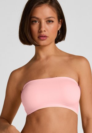 Young woman with short brown hair wearing a light pink strapless bandeau top, facing forward against a plain gray background.