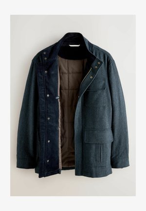 Granatowa kurtka w jodełkę z zamszowym kołnierzem, zamkiem błyskawicznym i zapięciem na zatrzask, oraz brązową pikowaną podszewką. Posiada kieszeń z przodu oraz detale wewnętrzne.