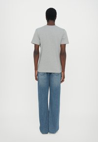 Tricou gri din bumbac cu mânecă scurtă, asortat cu blugi din denim albastru, cu talie înaltă și croială lejeră, văzut din spate.