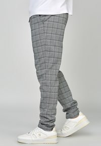 Pantalones a cuadros grises y negros hechos de tela ligera, corte ajustado, con bolsillos laterales y textura suave, combinados con zapatillas blancas.