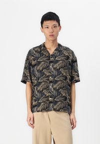 Camisa de manga corta negra con un patrón de follaje verde y dorado, con cierre de botones en la parte frontal y un corte relajado.