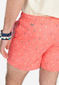 Bañador de coral hecho de tela ligera, con un patrón geométrico repetido en tonos azul claro, rosa y acentos grises. Cintura elástica.