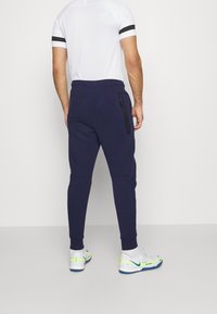 Navy joggers with tapered legs and zippered side pockets, paired with a white short-sleeve shirt with black accents, and white sneakers.