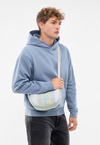 Borsa a tracolla con un gradiente pastello di blu, giallo e bianco. Tessuto morbido, forma rotonda e tracolla regolabile.