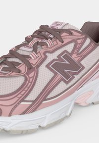 Близък план на розовo и бяло маратонка New Balance с кафяви връзки и горна част от текстуриран мрежест плат.
