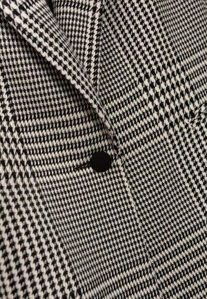 Czarna i biała tkanina w wzór houndstooth z pojedynczym czarnym guzikiem, ukazująca teksturowany, dopasowany design oraz ostre krawędzie klap.