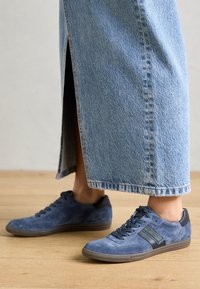 Blå mockasneakers med mörka accenter, snörningsdesign och texturerade sulor, kombinerade med en lång, ljus denimkjol.