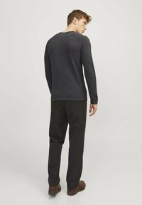 Camisa de manga larga gris oscuro con un acabado texturizado, combinada con pantalones negros y zapatos marrones, vista desde la parte trasera.