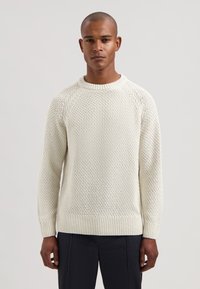 Pull en maille à col rond de couleur blanc cassé, présentant un motif texturé, des poignets et un ourlet côtelés. Confectionné dans un fil doux de poids moyen.