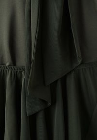 Dark green fabric with gathered seam detail and overlapping layers creating a textured, draped appearance.
