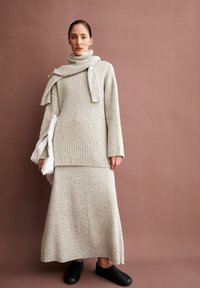 Strickpullover und langer Rock Set in Hellgrau mit gerippter Textur. Der Pullover hat einen Rollkragen und einen drapierten Schal. Schwarze Slipper.