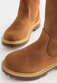 Bruine suède enkellaarsjes met een ronde neus, contrasterende stiksels en een chunky rubberen zool met gestructureerde loopdetails.