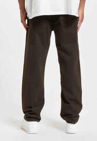 Pantalones de pierna ancha de color marrón oscuro, fabricados en algodón, con dos bolsillos traseros y una textura suave, combinados con zapatillas blancas.