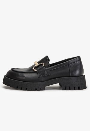 Sort læderloafer med kraftig rillesål og guldfarvet metalspænde, set fra siden på hvid baggrund.