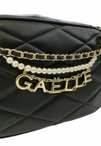 Borsa nera in ecopelle trapuntata con una tracolla in catena dorata con accenti di perle e un logo dorato "GAELLE" al centro.