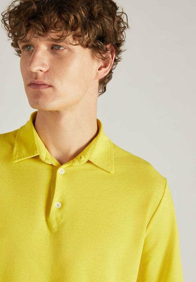 Geel poloshirt van zacht katoen, met een kraag en drie witte knopen aan de voorkant. Eenvoudig en effen kleur ontwerp.